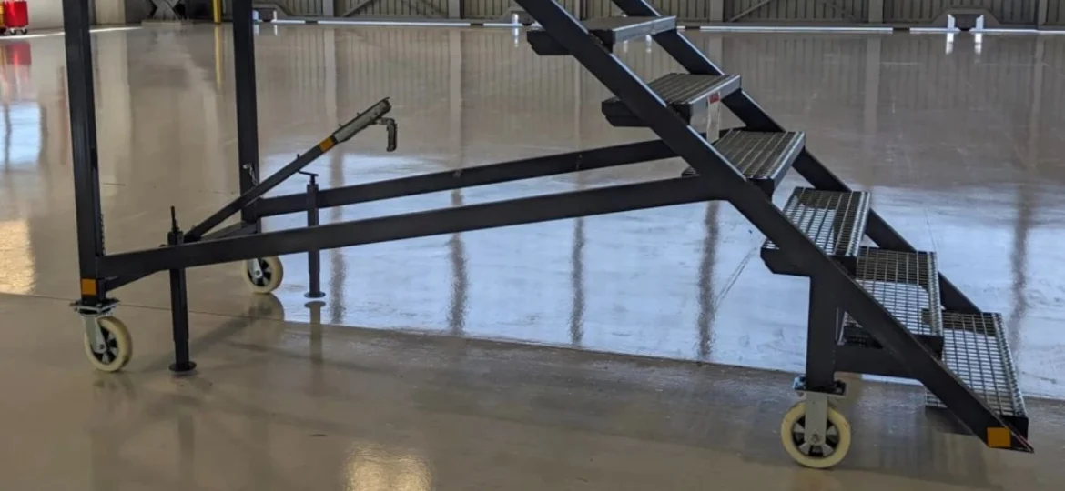 Premična kovinska stopnišča z nameščenimi industrijskimi kolesi za enostavno premikanje po proizvodni hali.