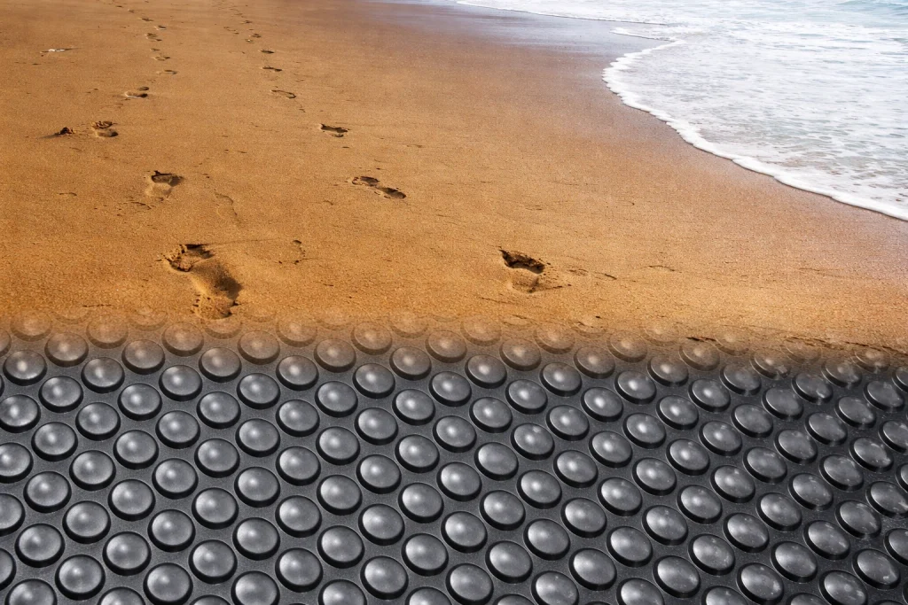 ergonomske-podloge-stopinje-v-pesku-header Stopinje v pesku in prehod na površino, kjer so ergonomske podloge za stanje.